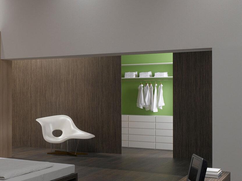 Schlafzimmerimpression von Bett, Nachtisch und Sideboard mit Holzverkleidung an Wand und indirektert Beleuchtung