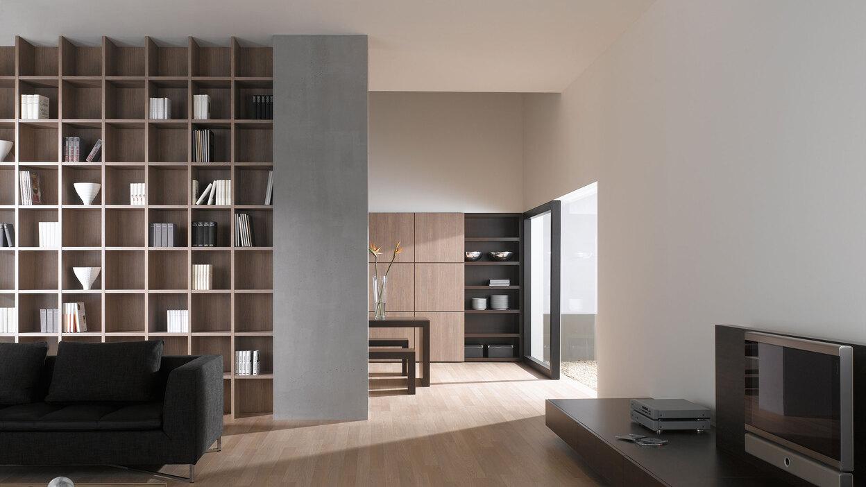 Offene Wohnraumimpression mit Einbauregal für Bücher und Dekoration in Trennwand mit hellem Holzboden