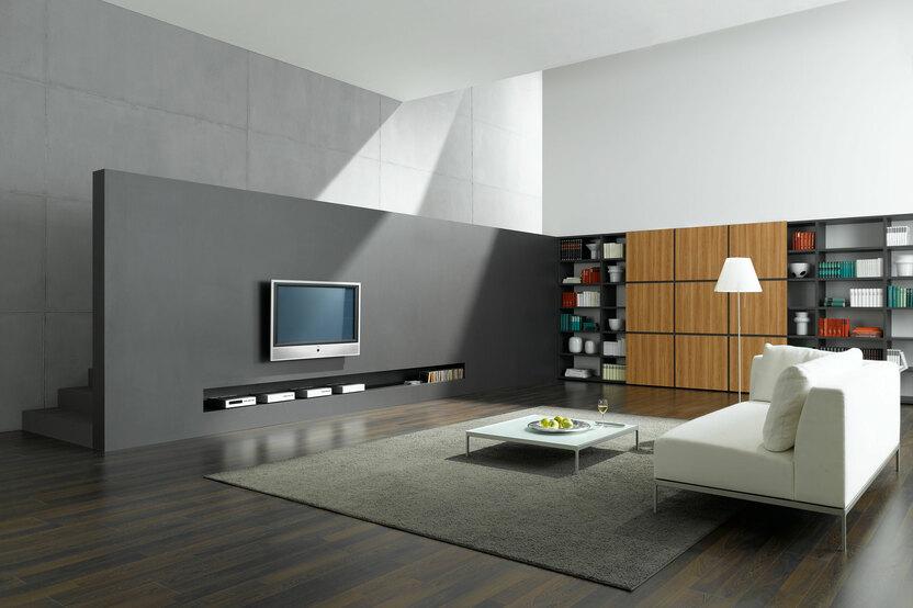 Offene Wohnraumimpression mit grauer TV-Trennwand zur Treppe und Einbauregal aus Holz und weißem Sofa