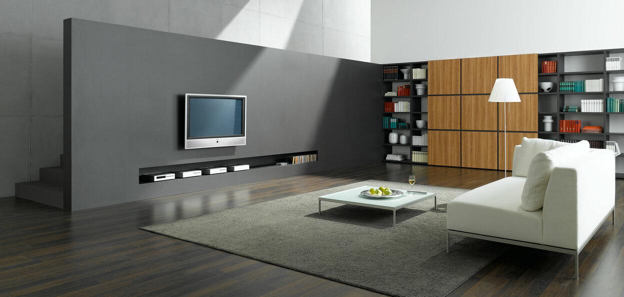 Wohnraumimpression mit Fernsehwand zur Treppe Offene Wohnraumimpression mit grauer TV-Trennwand zur Treppe und Einbauregal aus Holz und weißem Sofa