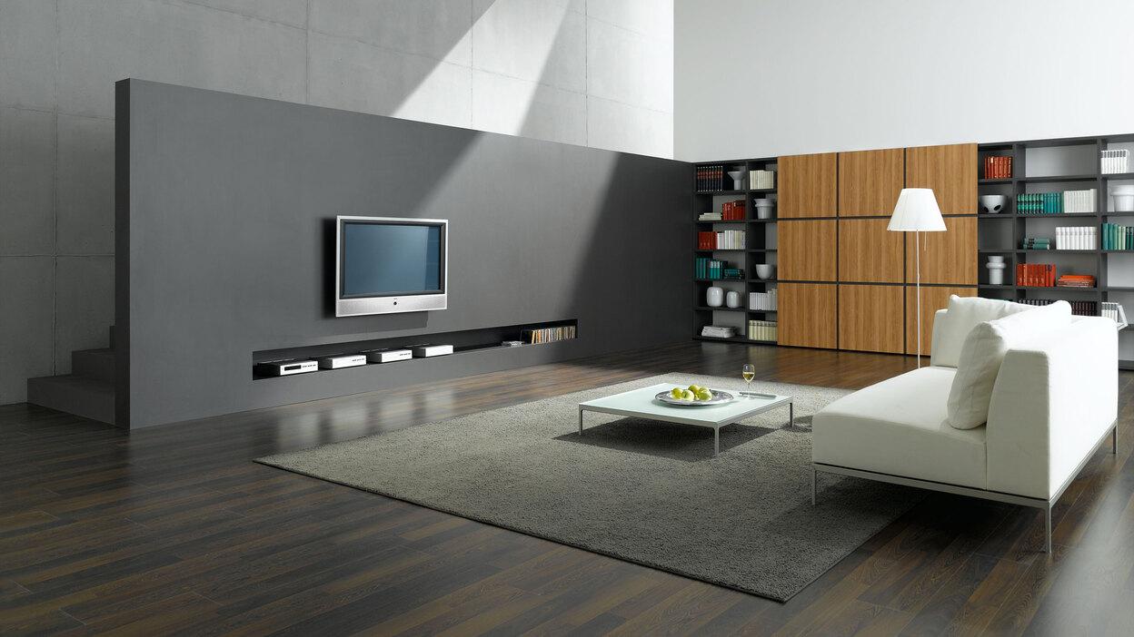 Offene Wohnraumimpression mit grauer TV-Trennwand zur Treppe und Einbauregal aus Holz und weißem Sofa